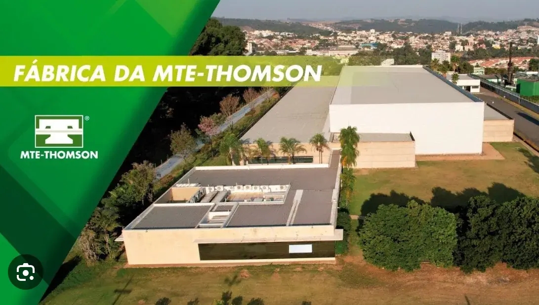 Aerial view of the MTE-THOMSON factory complex surrounded by greenery and the nearby town
