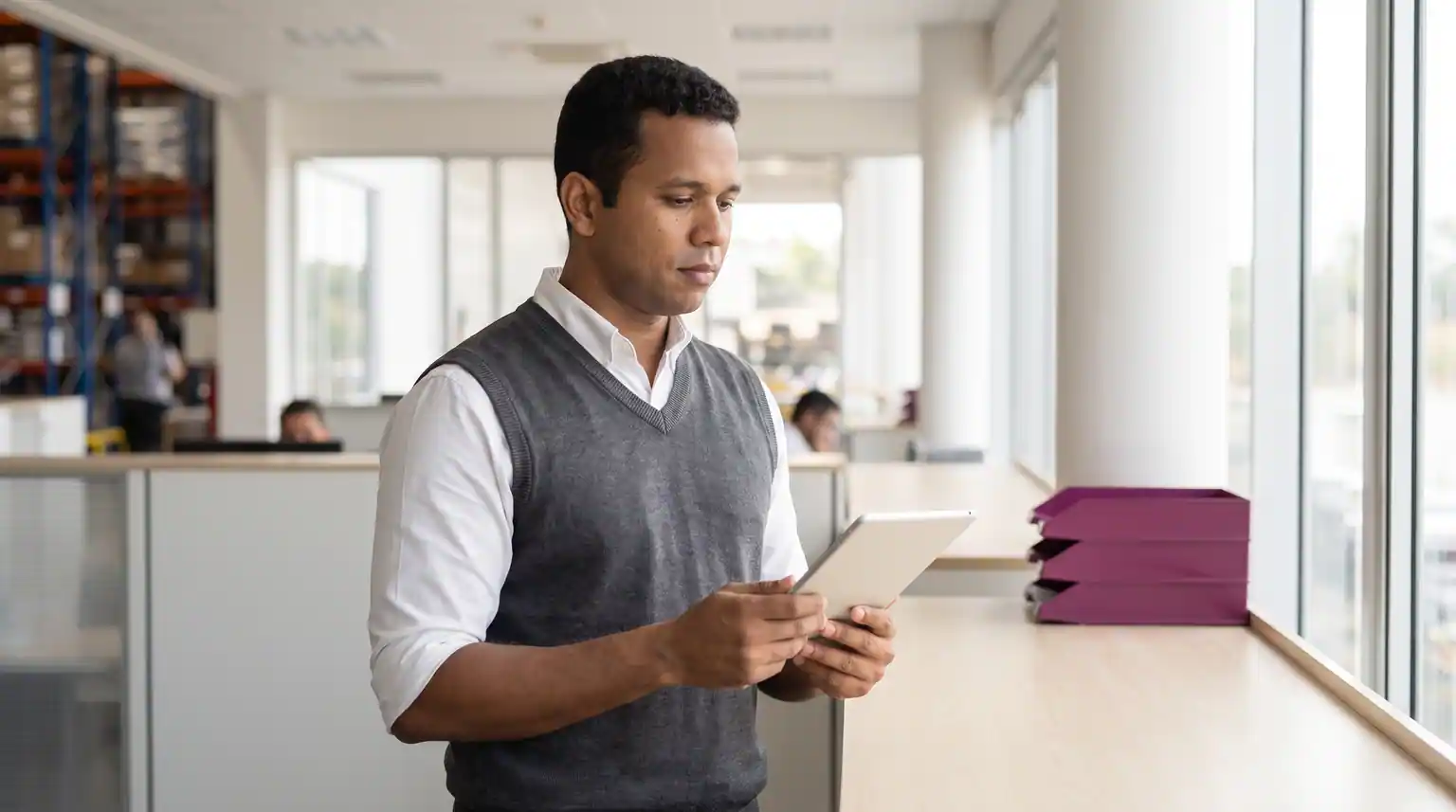 Vendedor B2B consulta pedidos num tablet perto da janela do escritório